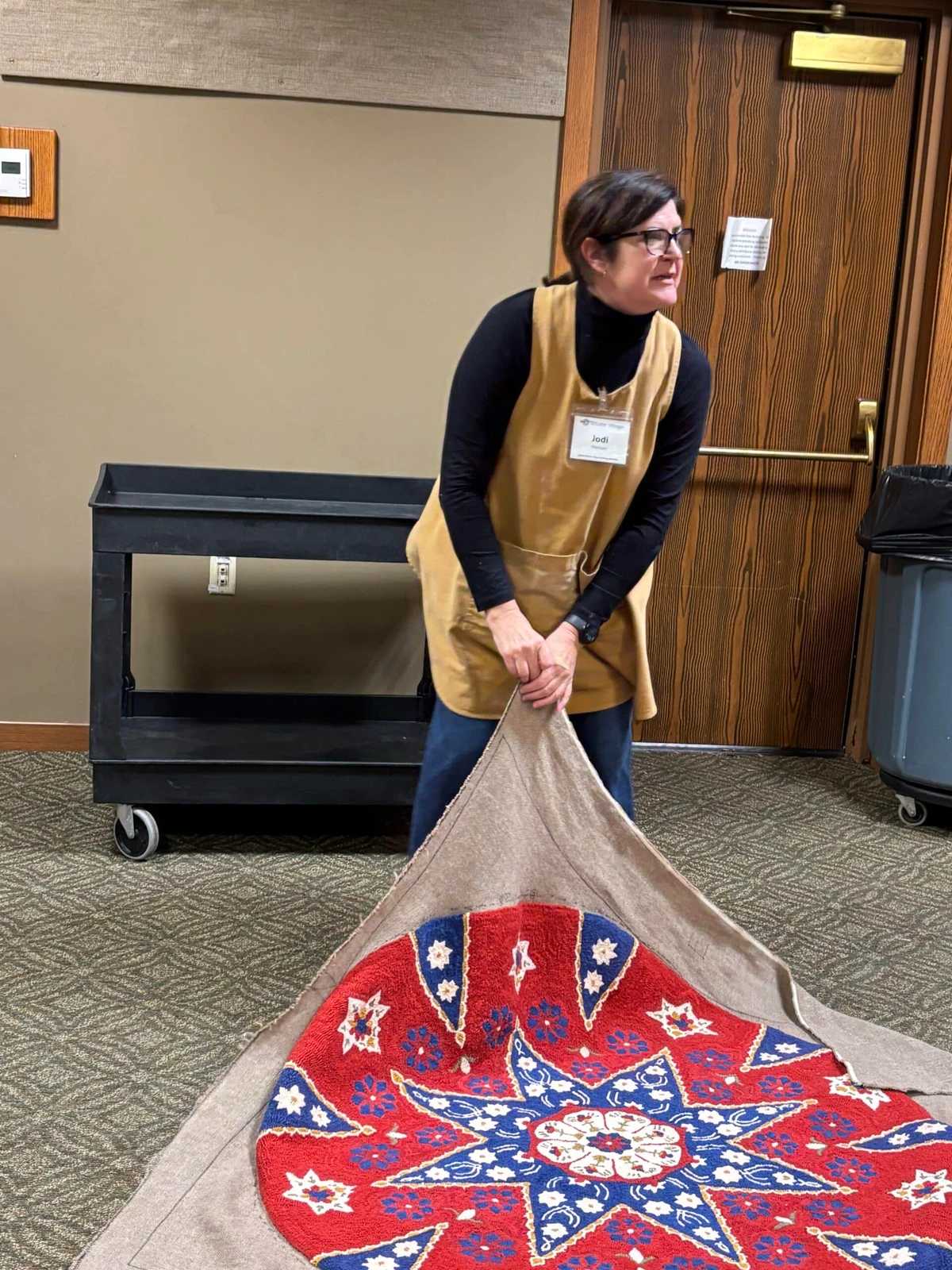 Jodi, a Sauder Village host, unfolds a colorful hooked rug during a rug-hooking retreat demonstration